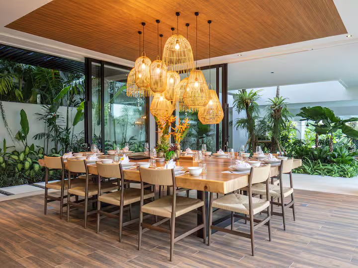 The villa's long teak dining table set under rattan pendant lights, open to the garden