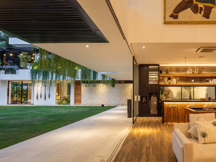 The villa's open-air lounge and bar glowing at dusk beside the lawn